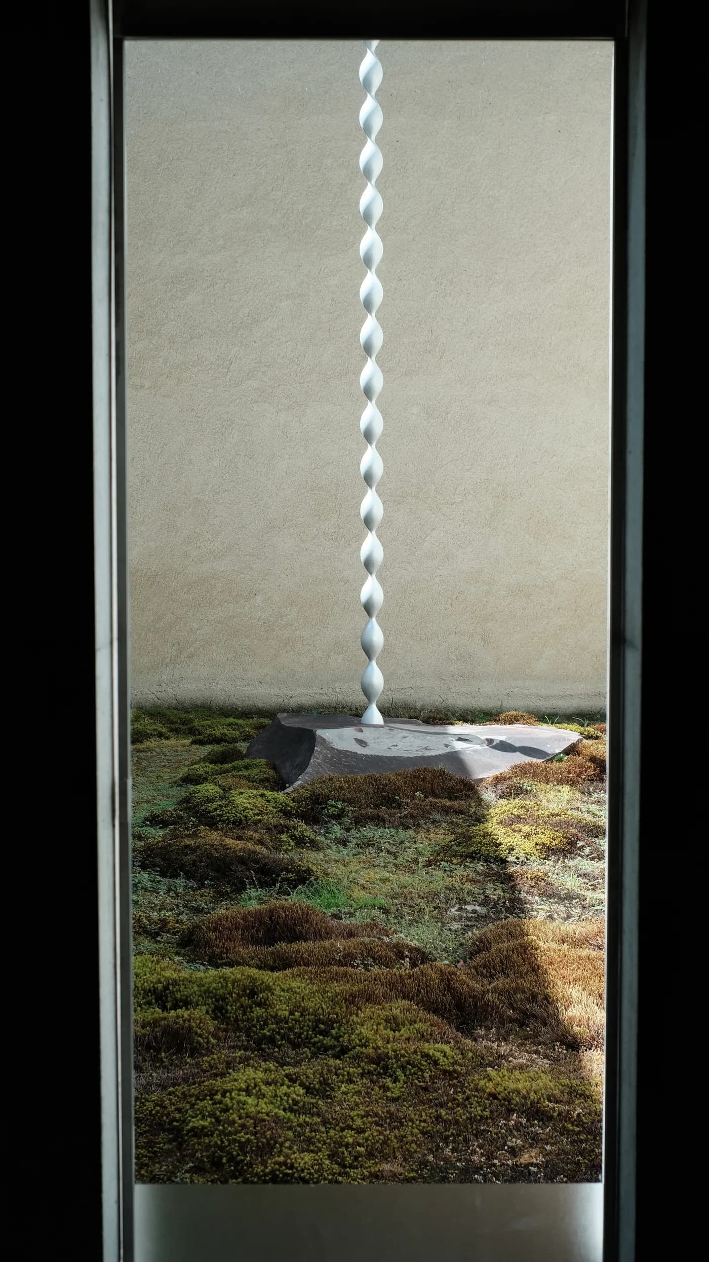 A white spiral installation and moss garden framed by a museum window